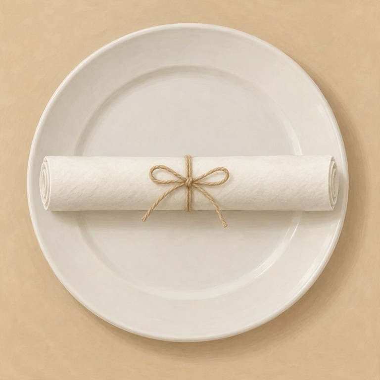 Rouleau de serviette blanche maintenu au milieu par un lien amovible et posé sur une assiette.