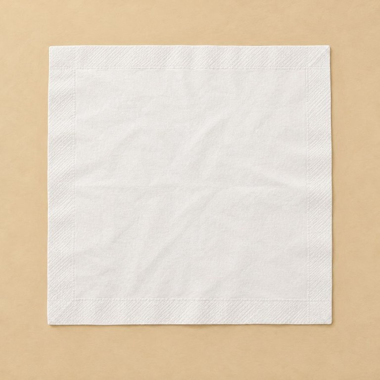 Serviette blanche carrée ouverte à plat sur une surface beige sèche.